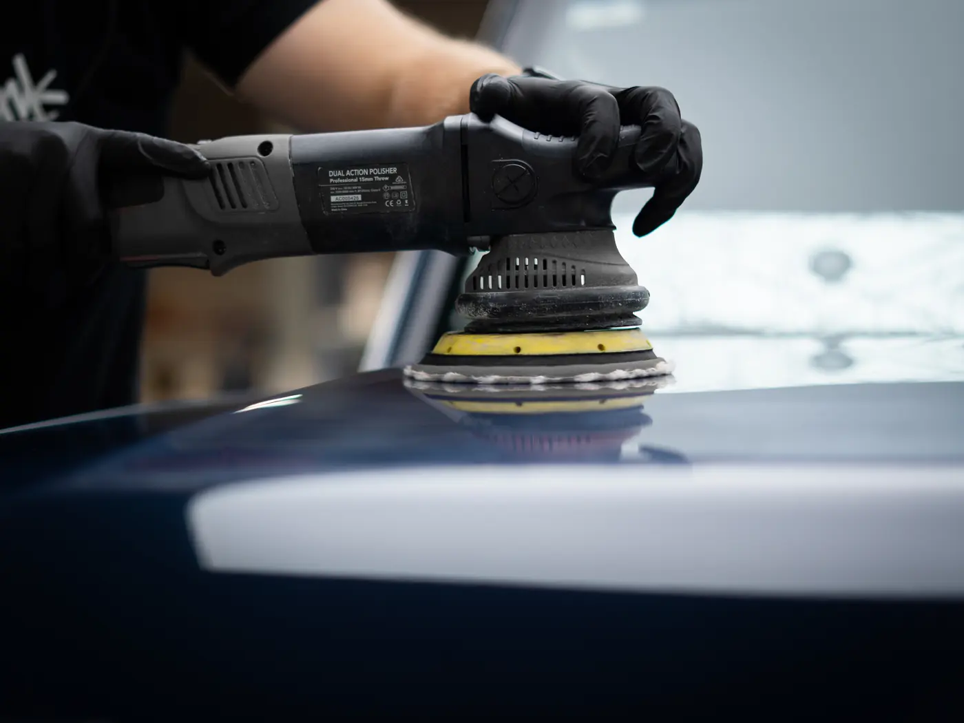 Technician machine-polishing a bonnet before ceramic coating