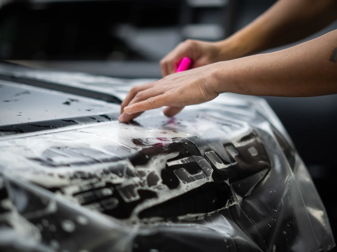 Installer smoothing protection film across a bonnet